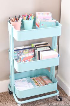 a blue rolling cart with two trays on it and various office supplies sitting on top