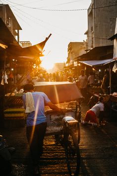 a person pushing a bicycle down a street with people in the background at sunset or dawn