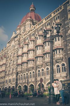 two people standing next to each other in front of a large building