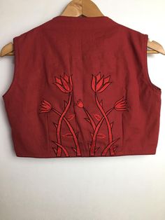 a red vest with flowers on it hanging from a wooden hanger in front of a white wall