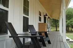 three chairs sitting on the front porch of a white house with wood siding and windows