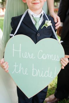 a young boy holding up a sign that says here comes the bride