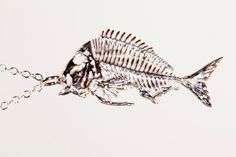 a fish skeleton is hanging from a chain on a white surface with water droplets around it