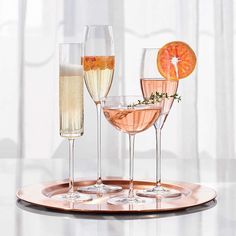 three wine glasses with orange slices and garnish on the rim, sitting on a tray