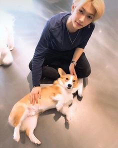 a woman kneeling down next to a brown and white dog on top of a floor