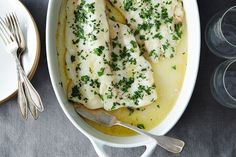 two fish fillets in a white dish with sauce and parsley on the side