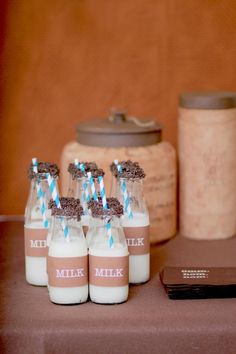 six milk bottles with blue and white straws in them sitting on a table next to a cell phone