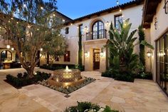 a courtyard with a fountain surrounded by greenery and lit up lights on the windows