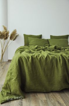 a bed with green sheets and pillows in a white room next to a plant on the floor