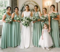 a group of women standing next to each other in front of a window holding bouquets