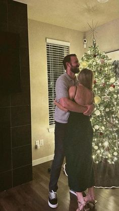 a man and woman hugging in front of a christmas tree