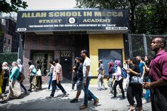 many people are walking on the sidewalk in front of a building with a sign that reads allaah school in medica street