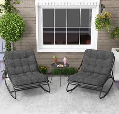 two chairs sitting next to each other in front of a brick wall with windows and potted plants