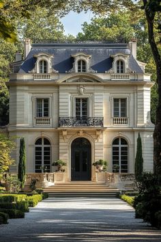 a large white house with lots of windows and bushes around it's front entrance