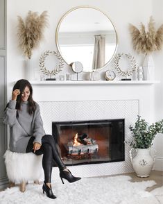 a woman sitting on a chair in front of a fireplace with a mirror above it