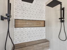 a bathroom with white tile and wood accents on the shower wall, along with two black hand held shower heads