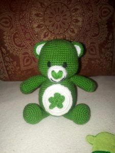 a green crocheted teddy bear sitting on top of a bed next to a turtle