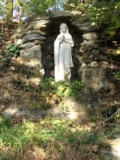 a statue is in the middle of some grass and rocks, with trees around it