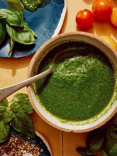 a bowl filled with green pesto next to some tomatoes and other vegetables on a table