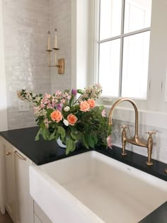 a white sink sitting under a window next to a black counter top with flowers in it