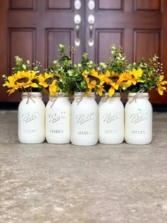 four mason jars with sunflowers and baby's breath are sitting in front of a door