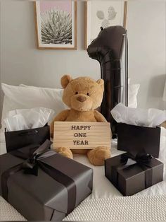 a brown teddy bear sitting on top of a bed next to two black wrapped presents