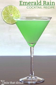 a green drink with a lime slice on the rim in a martini glass sitting on a table