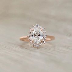 an oval cut diamond ring on top of a wooden table with the center stone surrounded by smaller round diamonds