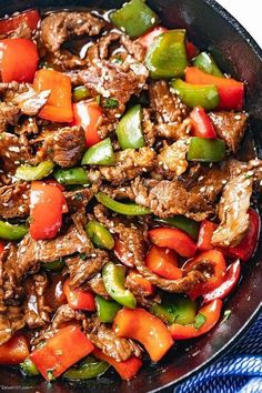 beef and peppers in a skillet on top of a blue towel with a fork