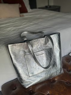 This exquisite Silver Everyday Tote is carefully crafted from luxuriously textured silver leather, accompanied with two shoulder straps. This timeless piece features a charcoal gray antigoccia coating interior lining and two interior zipper pocket for extra security, with an additional exterior zipper pocket. This everyday tote bag fits a 14" laptop, this handbag is crafted with Italian finesse and is the perfect everyday accessory. Silver Leather Tote Bag, Everyday Tote Bag, Luxe Jewelry, Everyday Tote, Everyday Accessories, Summer Accessories, Metallic Leather, Leather Earrings, Huggies Earrings