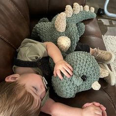 a little boy laying on top of a brown couch next to a stuffed dinosaur toy