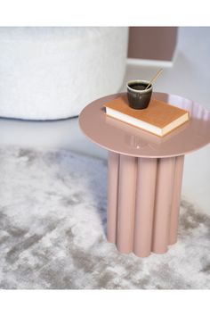 a small table with a book and a cup on it sitting on a carpeted floor