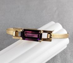 Classic AVON bangle bracelet.  Cast brass with the faux amethyst crystal center also being the clasp. Stone is 3/4 inches wide and about 1/3 inches tall. Prong set with open back to let light through. Bracelet is 3/8 inches tall and 6 1/2 inches long. The AVON marking is visible on the back of the stone setting. Stone Setting, Fort Myers, Amethyst Crystal, Stone Settings, Bangle Bracelet, Vintage Metal, Beautiful Earrings, Prong Setting, Cuff Bracelet