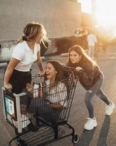 three young women pushing a shopping cart down the street while another woman stands next to them