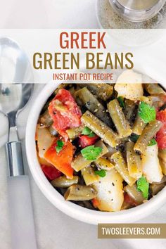 a white bowl filled with green beans and other vegetables on top of a table next to silver spoons