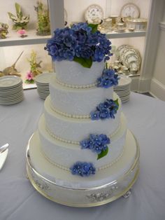 a three tiered cake with blue flowers on the top and bottom is sitting on a table