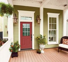 a red door on the side of a green house with white trim and wood flooring