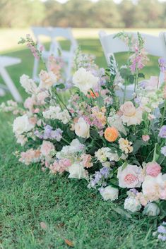 an arrangement of flowers and greenery on the ground at a wedding ceremony with white chairs in the background