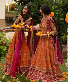 two women dressed in orange and pink outfits standing next to each other on the grass