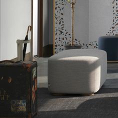 a white ottoman sitting in the middle of a room next to a suitcase and lamp