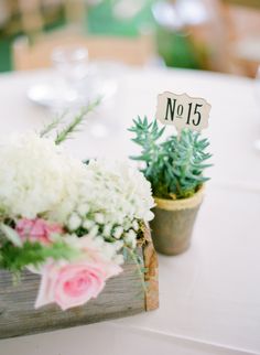 two small wooden planters with flowers on top of a white table cloth covered table