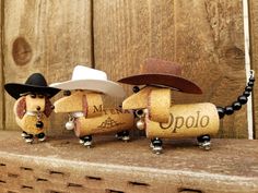 three little dogs wearing cowboy hats and holding wine corks on a wooden shelf with a chain