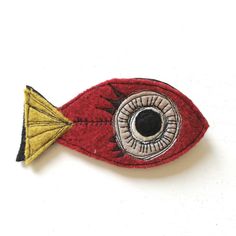 a close up of a red and yellow fish brooch with an eye on it