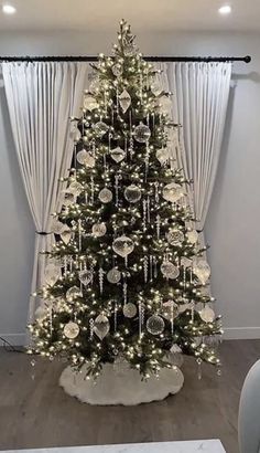 a decorated christmas tree in front of a window with white curtains and lights on it