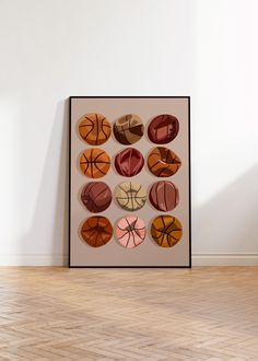 a framed photograph of basketballs in different colors on a white wall with hardwood flooring