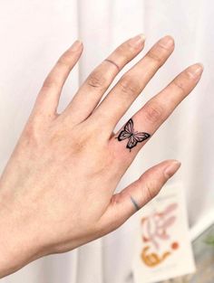 a woman's hand with a small butterfly tattoo on the middle finger and ring