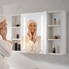 a woman is looking at her reflection in the mirror while she brushes her teeth with a towel on her head