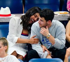 a man and woman sitting next to each other at a tennis match, one holding his arm around the other's shoulder