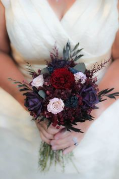 a bride holding a bouquet of red and purple flowers on her wedding day at the same time