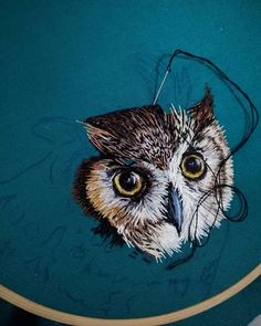 an owl's head is painted on a piece of fabric in the shape of a hoop